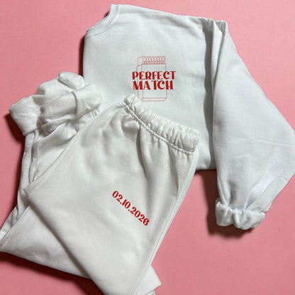 White sweatshirt and pants with red text on a pink background