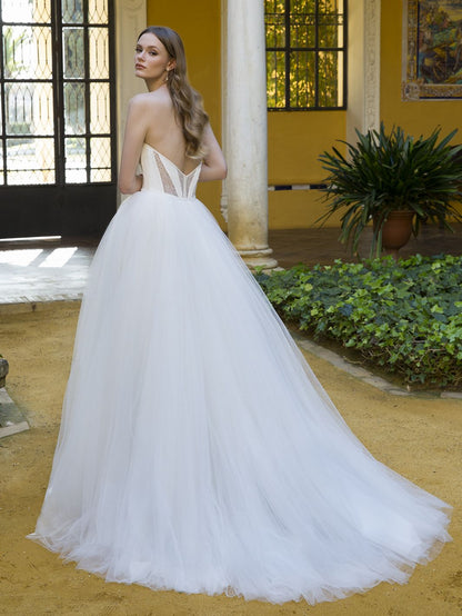 Woman in a white wedding dress standing in an outdoor setting with columns and plants.