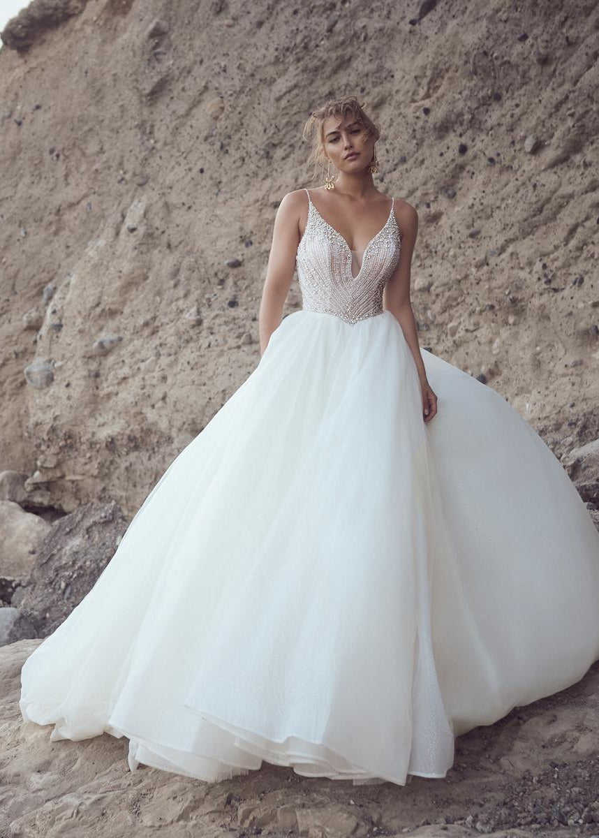 Woman in a white wedding dress standing on a rocky beach with a mountainous background
