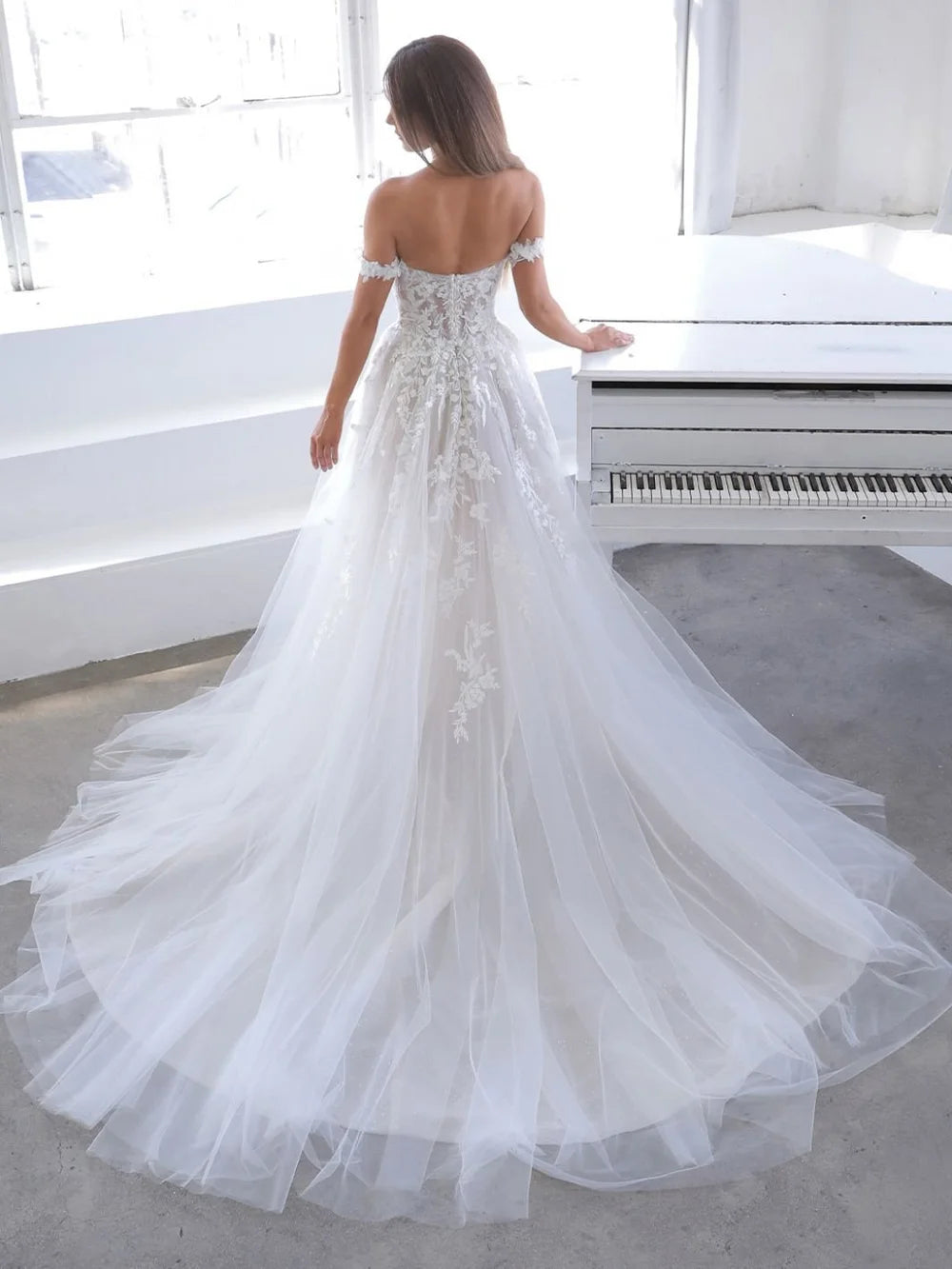 Woman in a white wedding dress standing in a room with a piano.