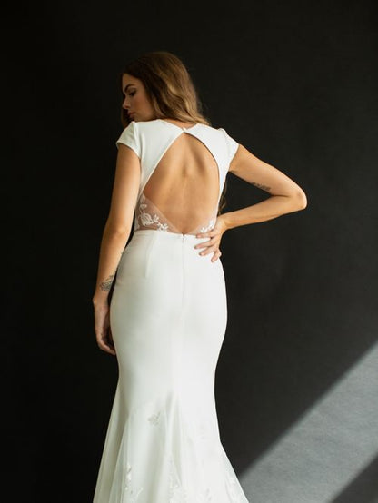 Brie is classic and timeless. Made of stunning crepe fabric, she has a bateau neckline falling into small cap sleeves. Her fitted silhouette lows into a gorgeous lace train, with a keyhole back.