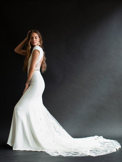 Brie is classic and timeless. Made of stunning crepe fabric, she has a bateau neckline falling into small cap sleeves. Her fitted silhouette lows into a gorgeous lace train, with a keyhole back.