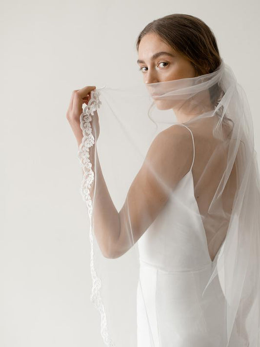 Woman wearing a white wedding dress with a sheer veil against a plain background