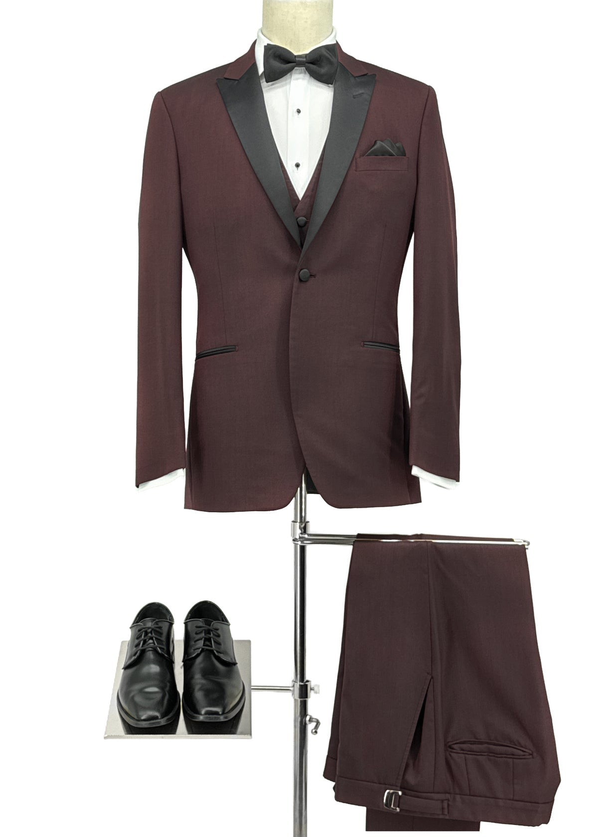 Maroon tuxedo with black lapels and bow tie on a mannequin, paired with black shoes and pants on a white background.