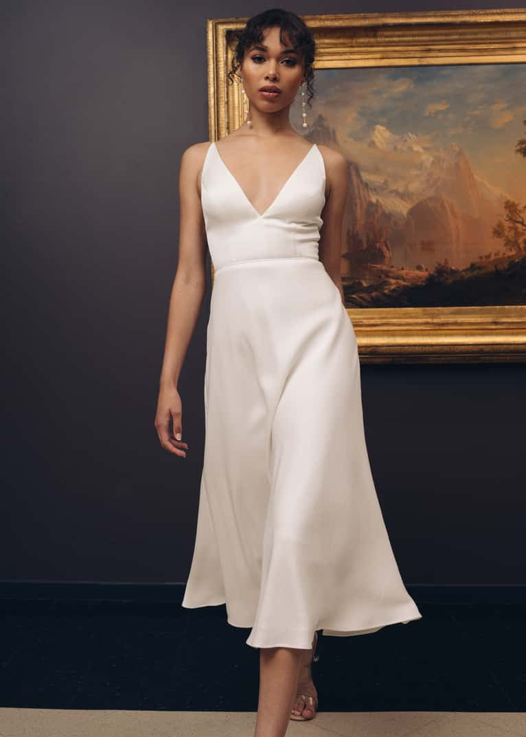 Woman in a white dress standing in front of a painting with a dark wall background
