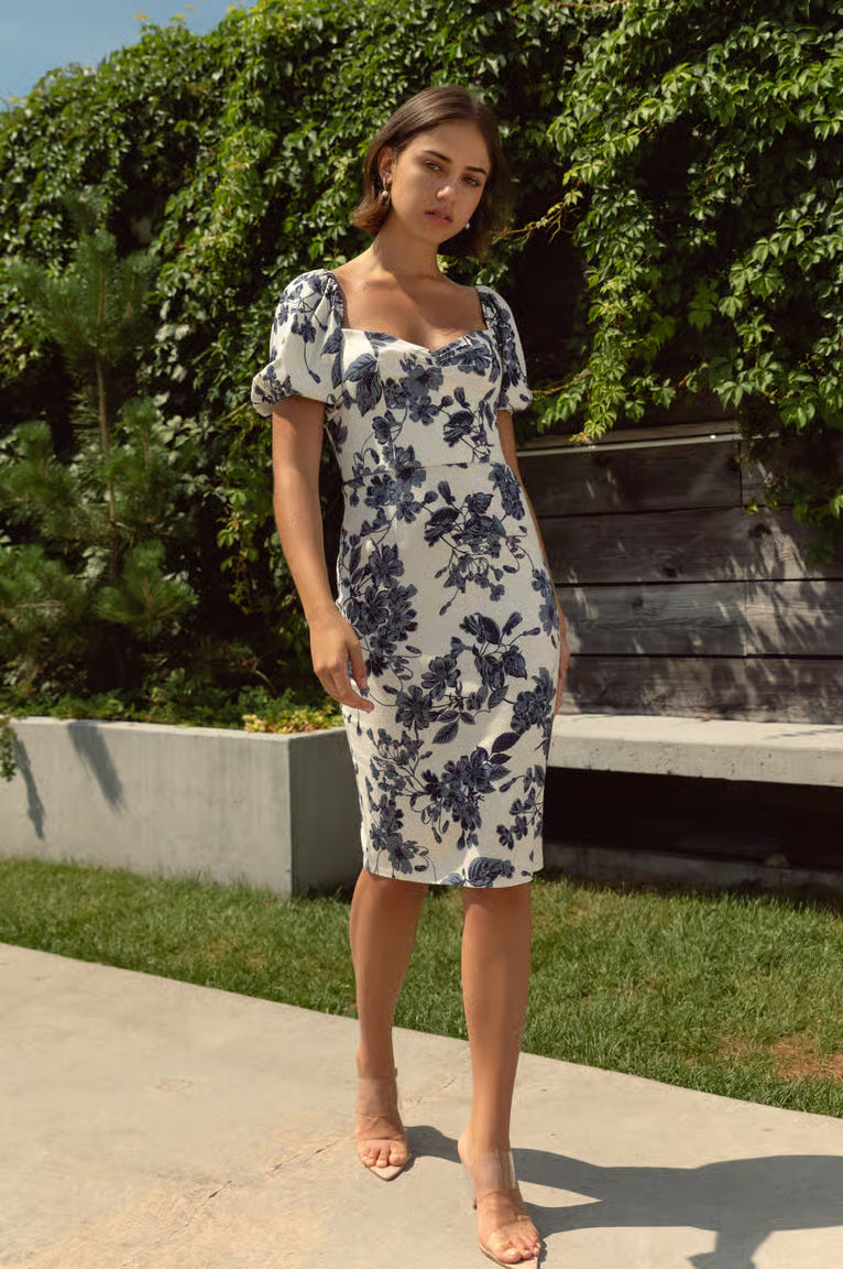 Woman wearing a floral dress standing outdoors with greenery in the background