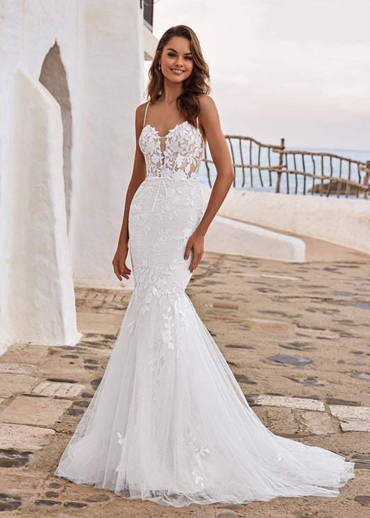 Woman in a white lace wedding dress standing on a stone path with a scenic background.