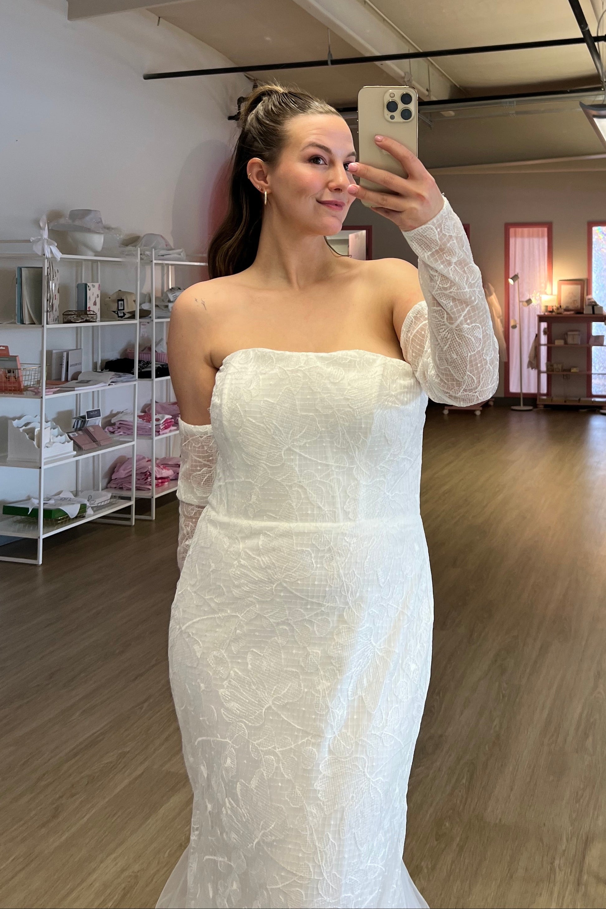 Abby taking a mirror selfie at NKIN, off the rack bridal shop, wearing a white strapless dress , the Elvira, in the NKIN showroom 