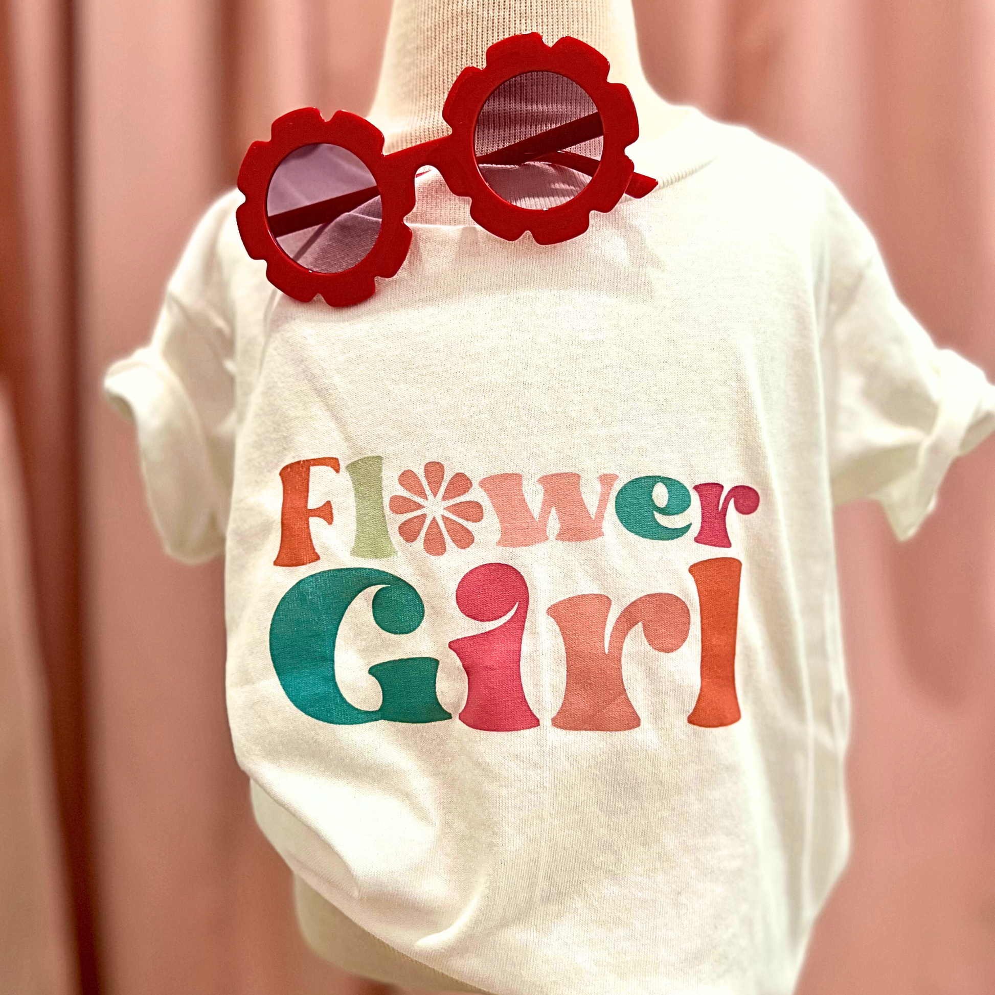 White t-shirt with 'Flower Girl' text and red sunglasses on a plain background