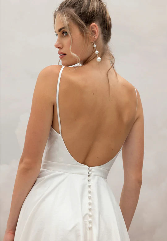 Woman wearing a white dress with an open back on a plain background