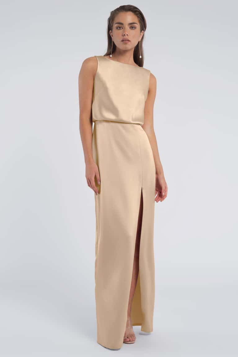 Woman wearing a beige sleeveless gown with a slit on a light gray background