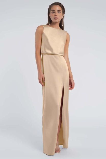 Woman wearing a beige sleeveless gown with a slit on a light gray background