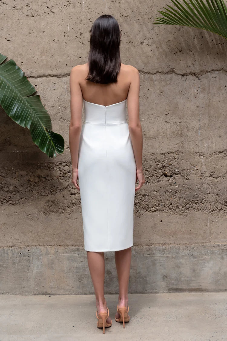 Woman wearing a white strapless dress standing against a textured wall.