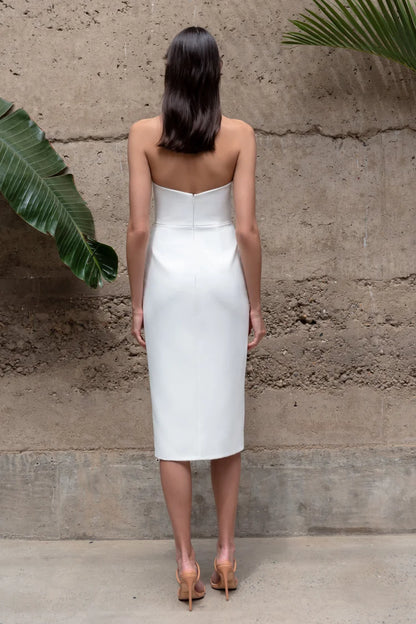 Woman wearing a white strapless dress standing against a textured wall.