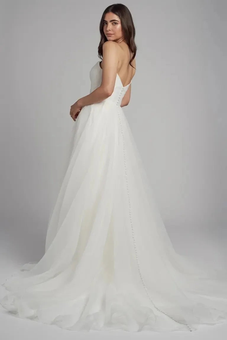 The Bronte bridal gown is cut in our lighter than air pebbled organza fabric. The flattering scoop neck is accented by the beautifully pleated bodice and elegantly draped sleeves which can be removed to create a strapless look. The full A line skirt lends a whimsical yet dramatic feel to this timeless gown.