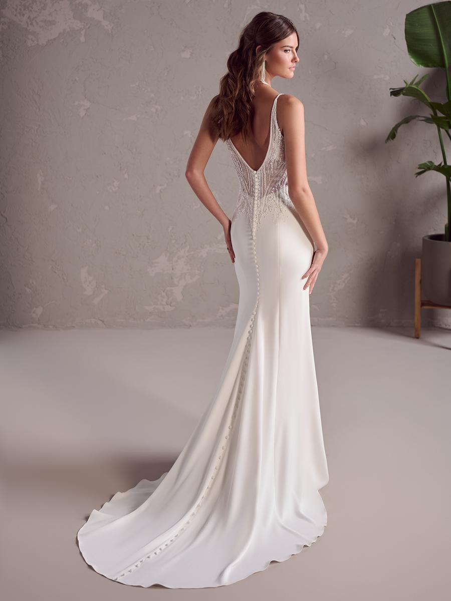 Woman wearing a white wedding dress with a lace back in a minimalistic setting.