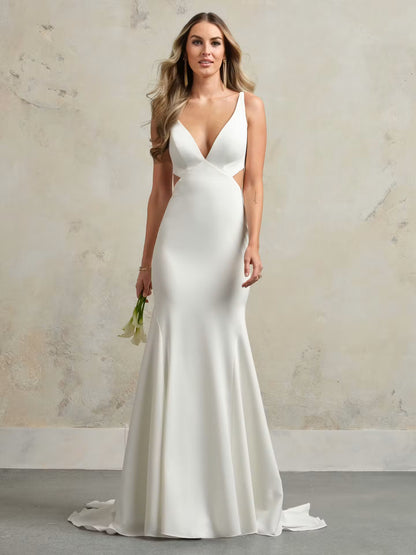 A woman modeling a floor-length white satin gown with a deep V-neckline, side cutouts, and a slight train, standing against a textured beige wall.