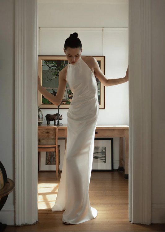 The Laurene is a bias-cut silk blend dress featuring a high collar and open back. Adorned with pleats in the front, a leg slit and jaw dropping open back design. A detachable bow in the back finished off this relaxed fit timeless gown.


The Laurene dress is classic yet modern, elegant but sexy. It will be perfect for a beach wedding, city-chic ceremony, or any wedding-related events such as elopement, rehearsal dinner, or reception.