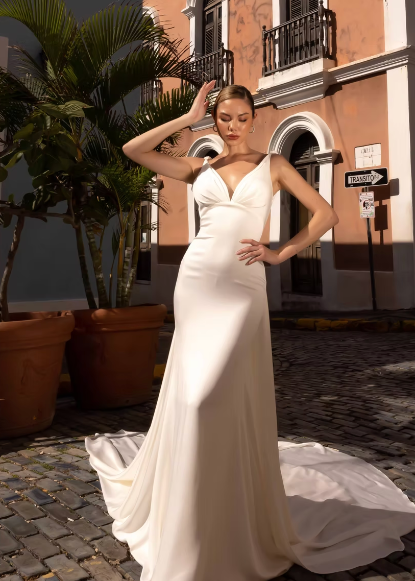 Woman in a white wedding dress standing on a cobblestone street with buildings and plants in the background.