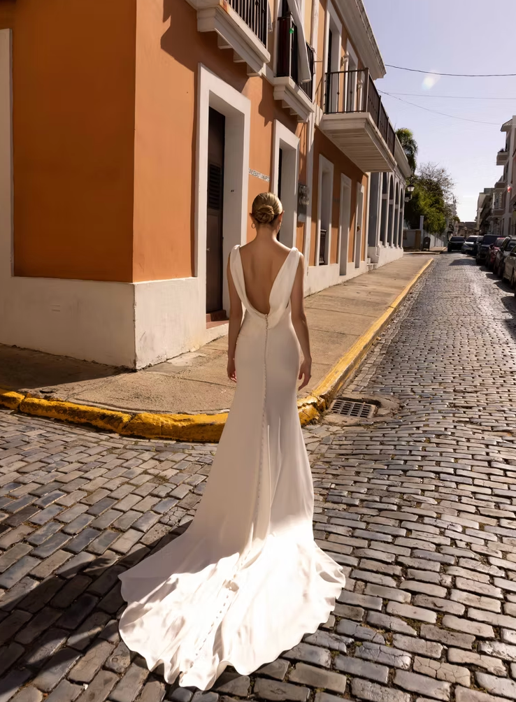 Woman in a white wedding dress walking down a sunlit street with buildings on either side.