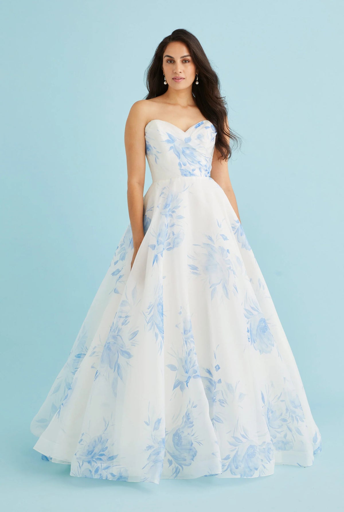 A woman modeling a strapless white ball gown with a sweetheart neckline and light blue floral print, set against a solid light blue studio background.