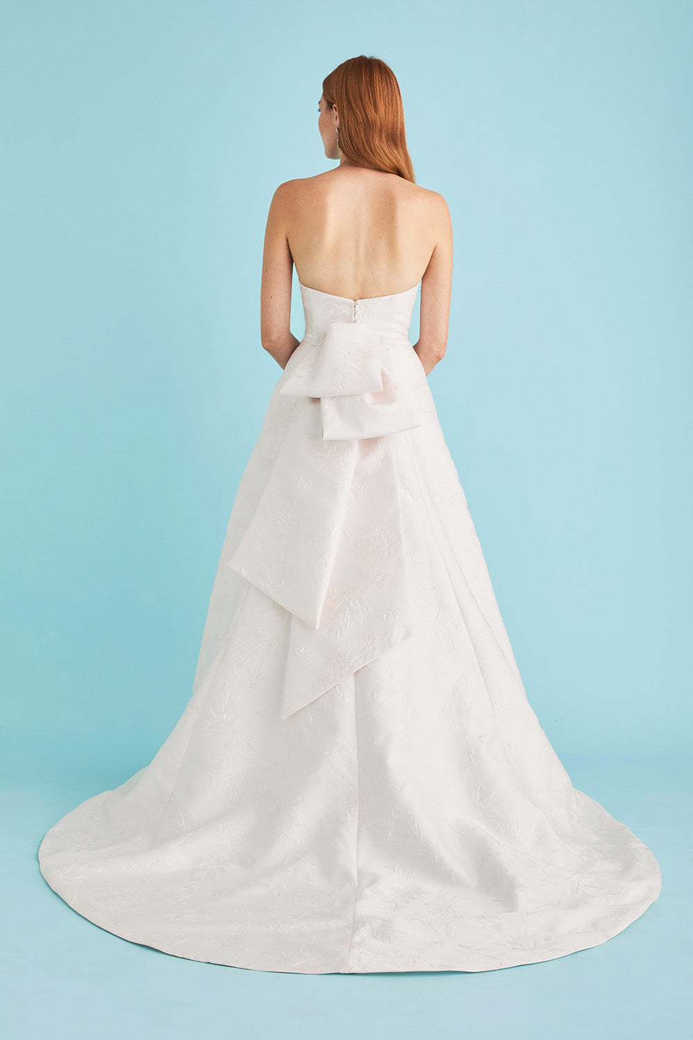 White strapless wedding dress with a large bow on a light blue background