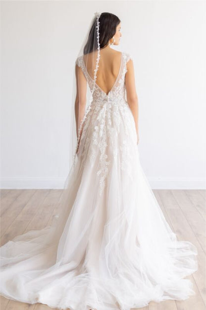 White wedding dress with a long train and lace detailing on a plain background