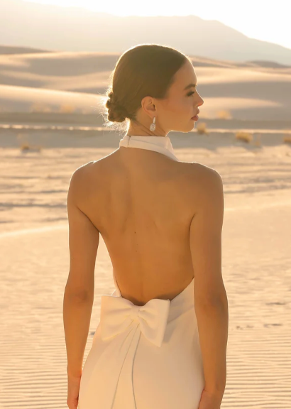 Woman in a white dress with an open back standing in a desert landscape.