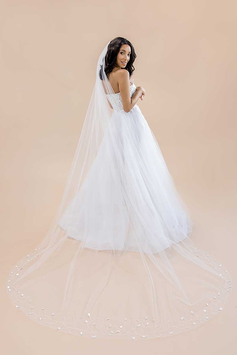 Woman wearing a white wedding dress with a long veil against a beige background