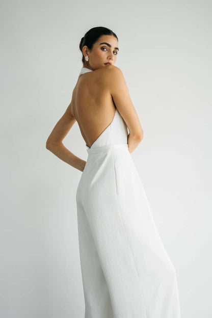 Woman wearing a white wedding jumpsuit with an open back against a plain background