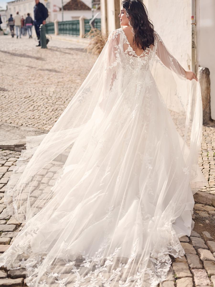 Woman in a white wedding dress with a long train on a cobblestone street.