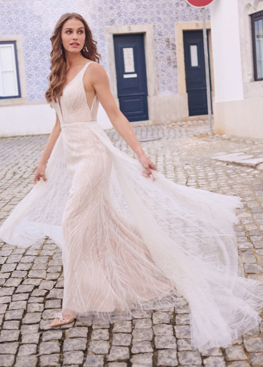 Woman in a white wedding dress standing on a cobblestone street with blue doors in the background.
