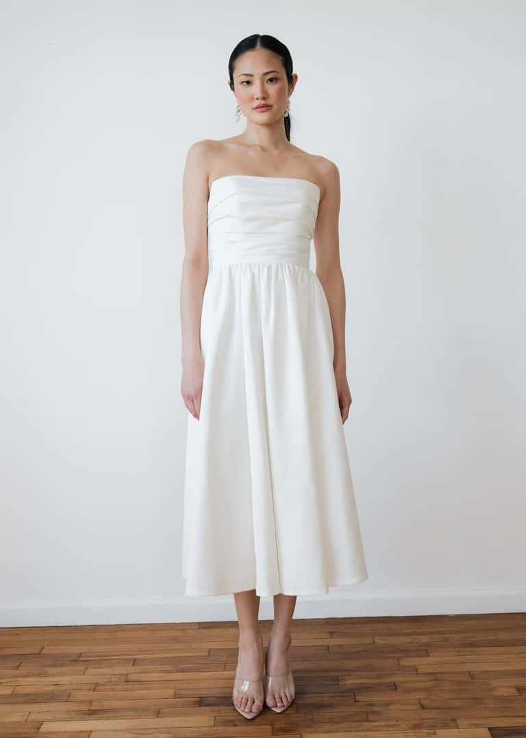 Woman wearing a strapless white dress against a plain white wall.