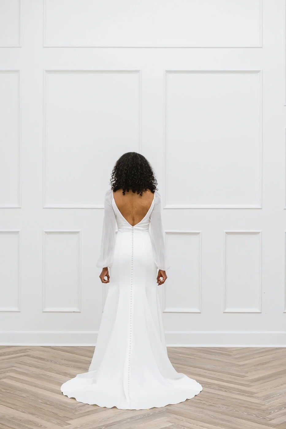 Person wearing a white wedding dress with a deep backless design in a minimalistic setting.