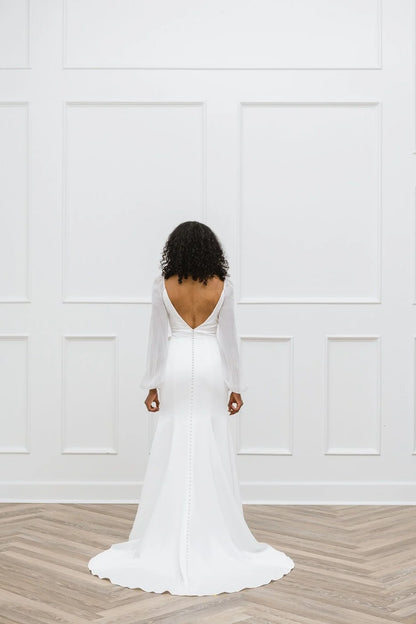 Person wearing a white wedding dress with a deep backless design in a minimalistic setting.