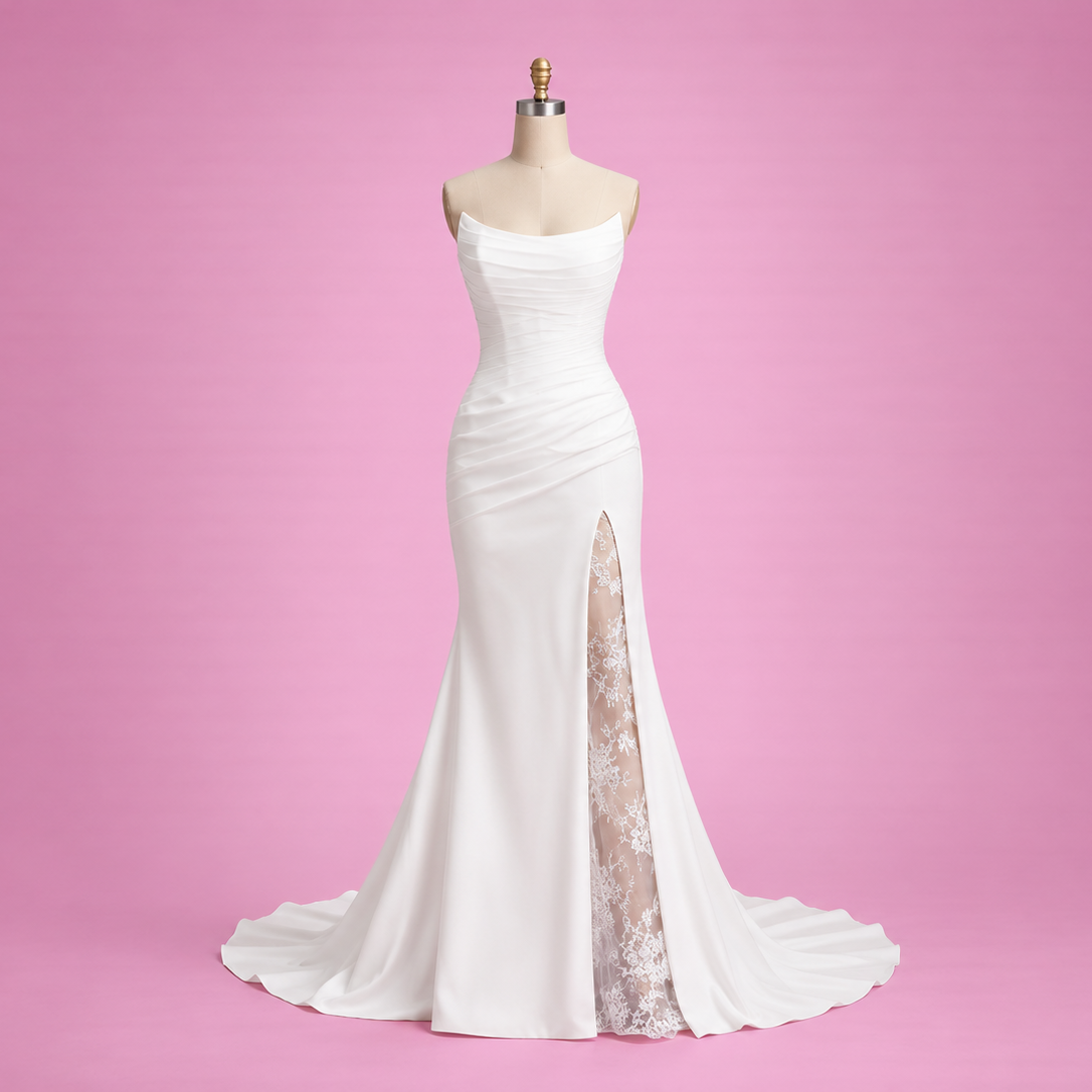 A white strapless mermaid-style evening gown displayed on a dress form against a solid pink studio background. The dress has a fitted bodice, a high slit with sheer nude lace lining, and a slight train.