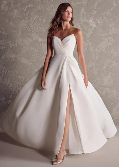 Woman wearing a white strapless gown with a high slit on a textured wall background