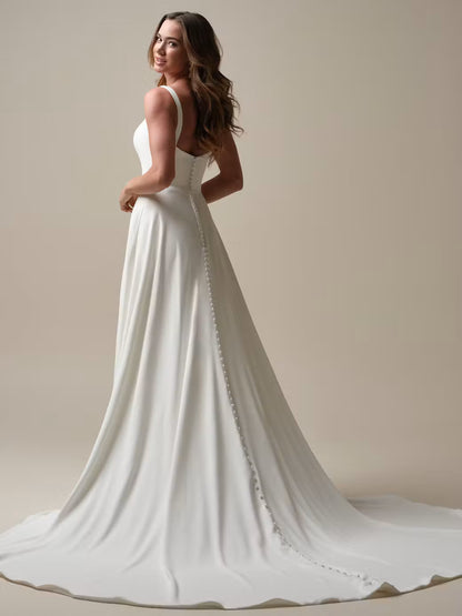 Woman wearing a white wedding dress with a long train against a neutral background