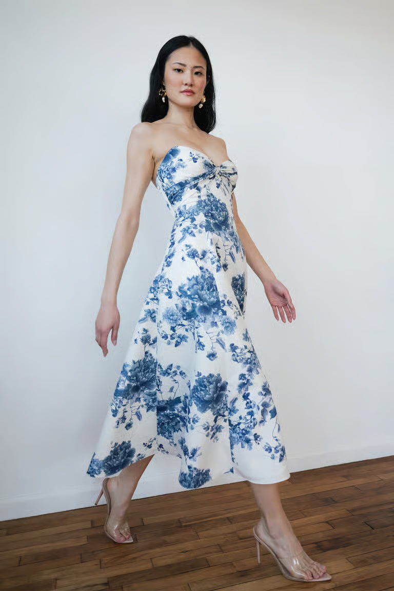 Woman wearing a strapless floral dress against a white wall.