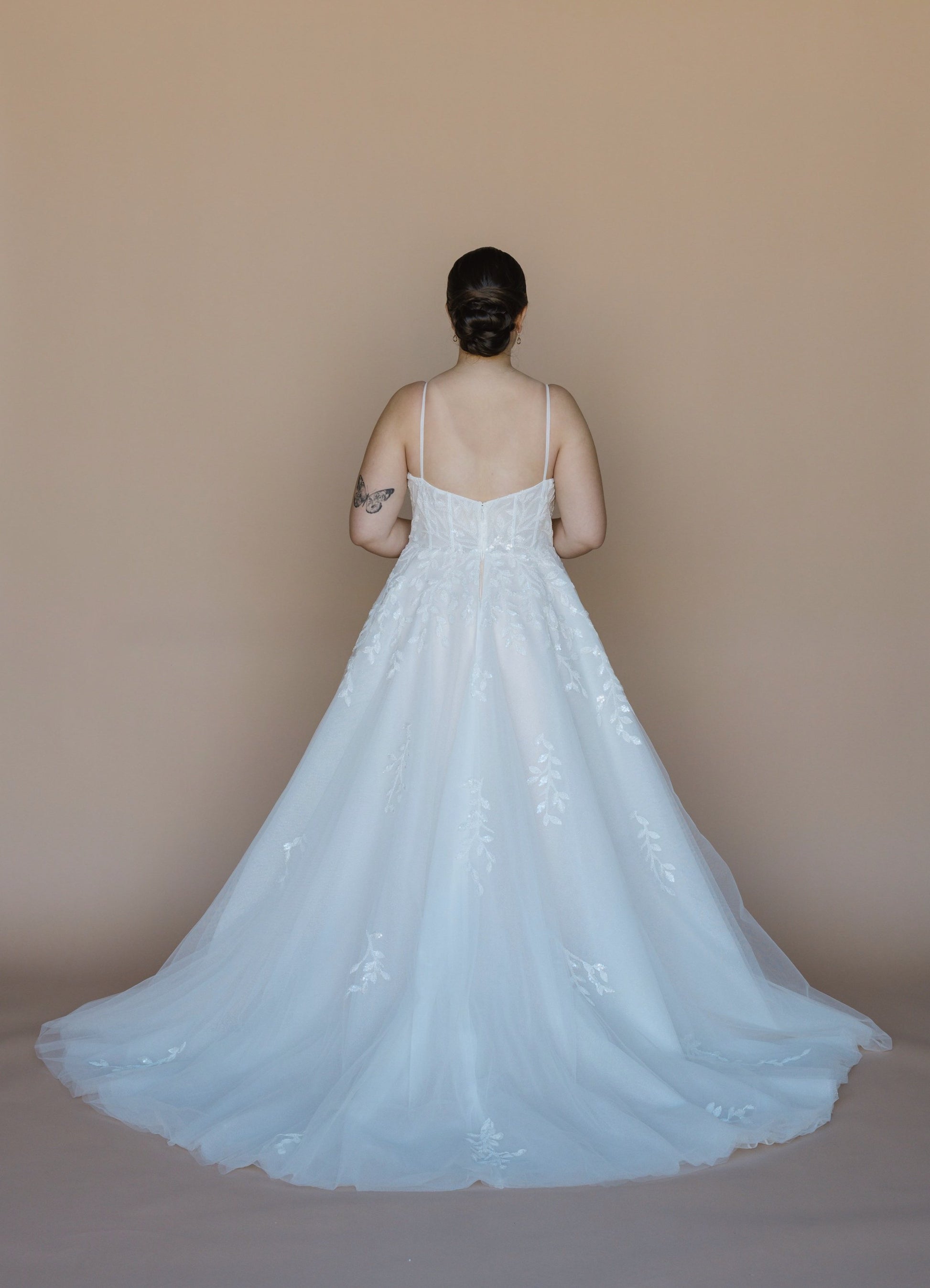 Person wearing a white lace wedding dress against a plain background