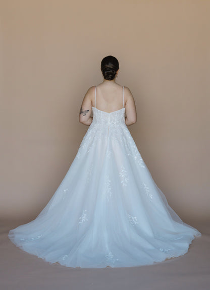 Person wearing a white lace wedding dress against a plain background