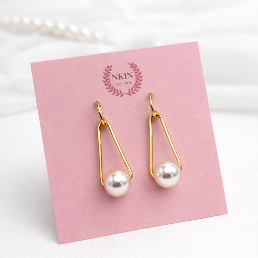 Gold earrings with pearls on a pink card with 'NKIN branding.