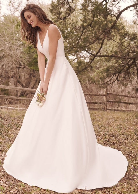 Woman in a white wedding dress standing in a natural setting with trees and a wooden fence.
