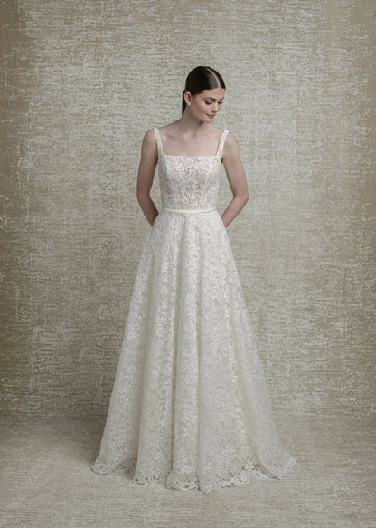 Woman wearing a lace wedding dress against a textured beige wall