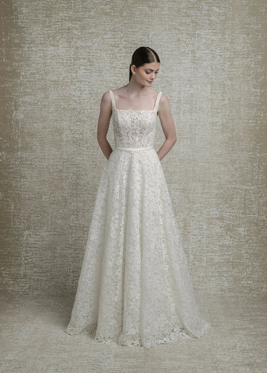 Woman wearing a lace wedding dress against a textured beige wall