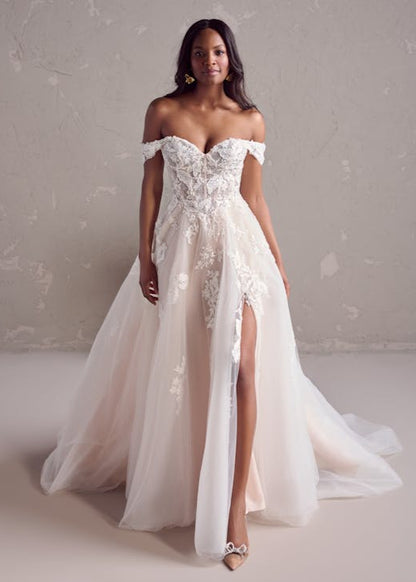 Woman wearing a white off-shoulder lace wedding dress with a high slit on a plain background