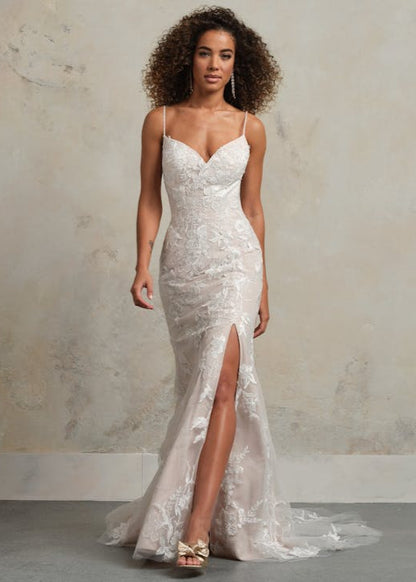 Woman wearing a white lace wedding dress with a slit on a plain background