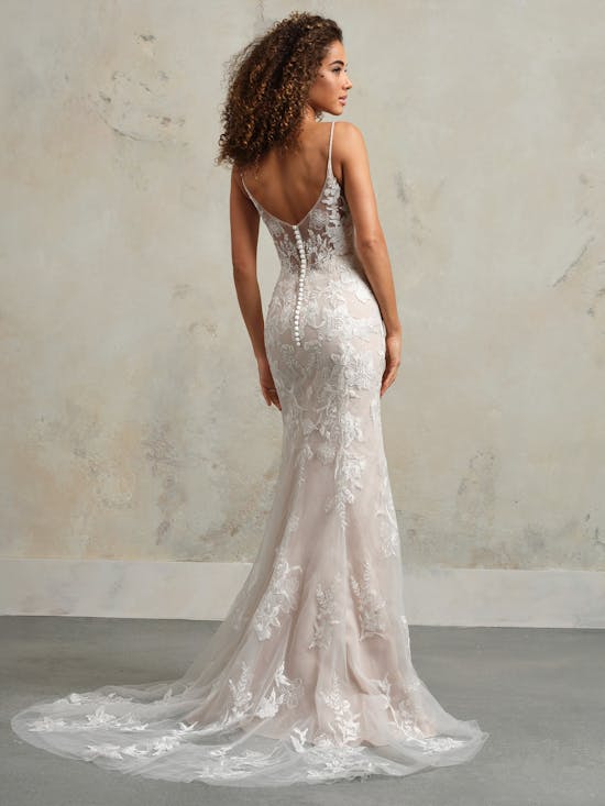 Woman wearing a white lace wedding dress with a long train against a neutral background