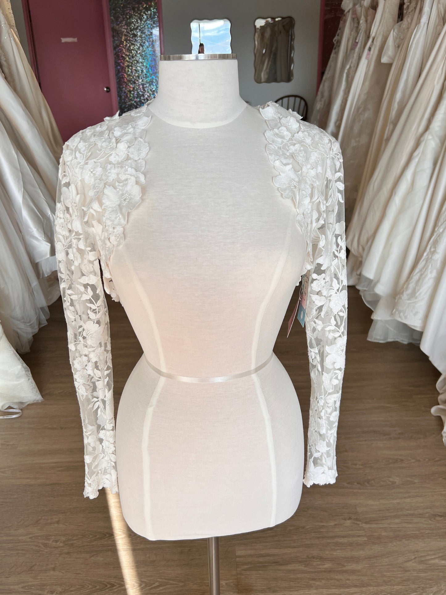Mannequin wearing a white wedding dress with lace details in a store setting.