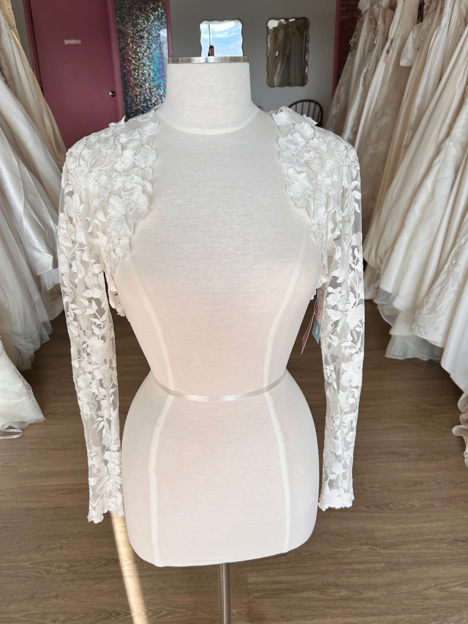 Mannequin wearing a white wedding dress with lace details in a store setting.